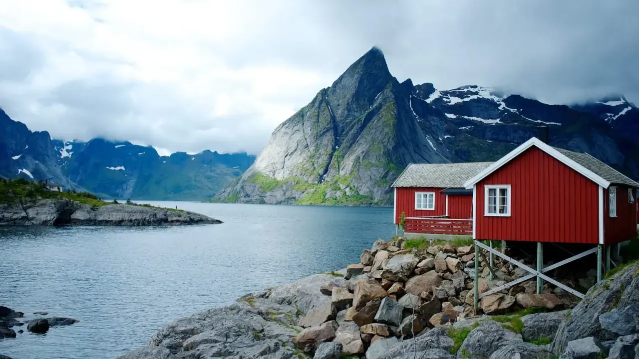 Två röda stugor vid en sjö med dramatiska berg i bakgrunden. Perfekt för att vandra i Norge.