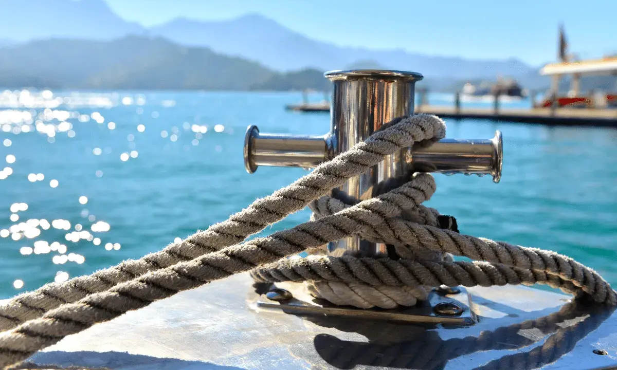 Corde épaisse enroulée autour d'une bitte d'amarrage en acier inoxydable. Le soleil brille sur l'eau bleue. Cela illustre comment fonctionne une ancre de bateau.