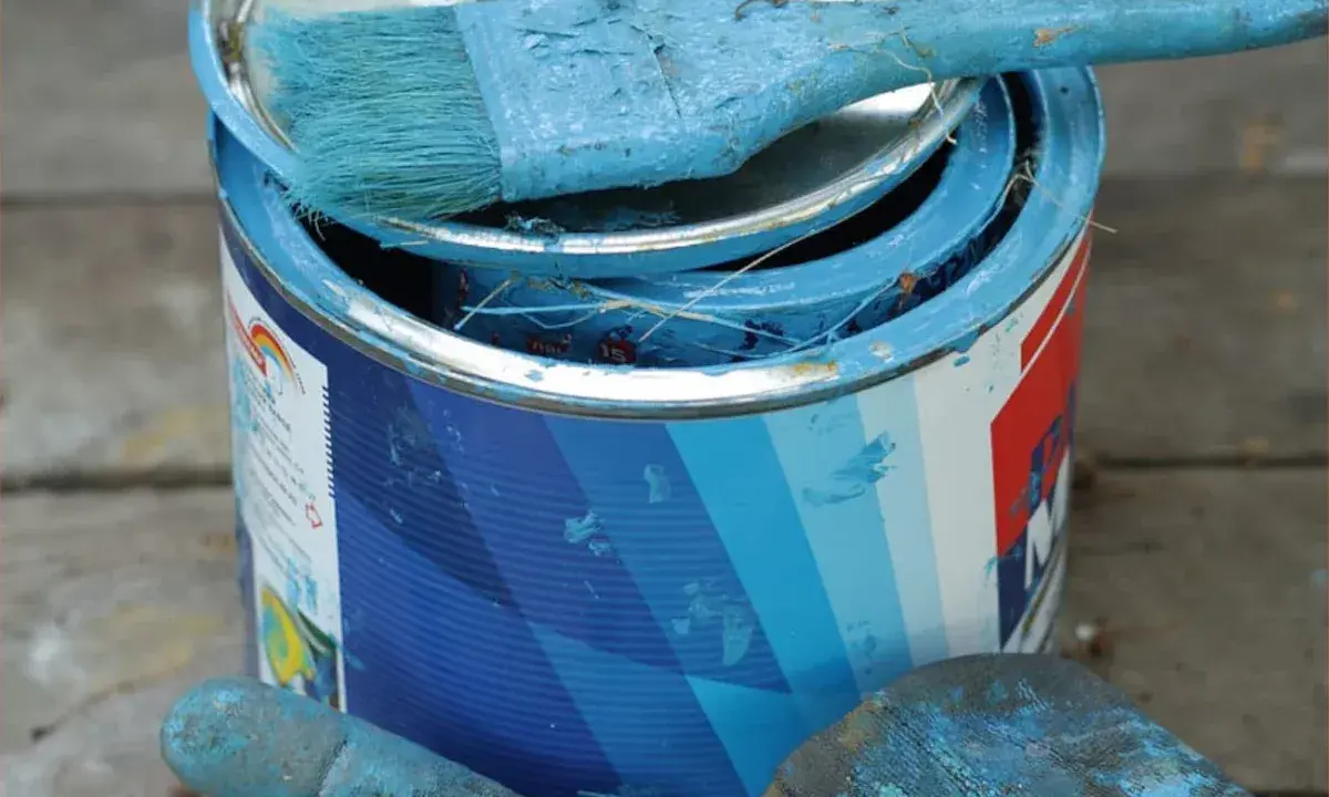Puszka z niebieską farbą plakatową, pędzel i rękawica pokryte farbą.