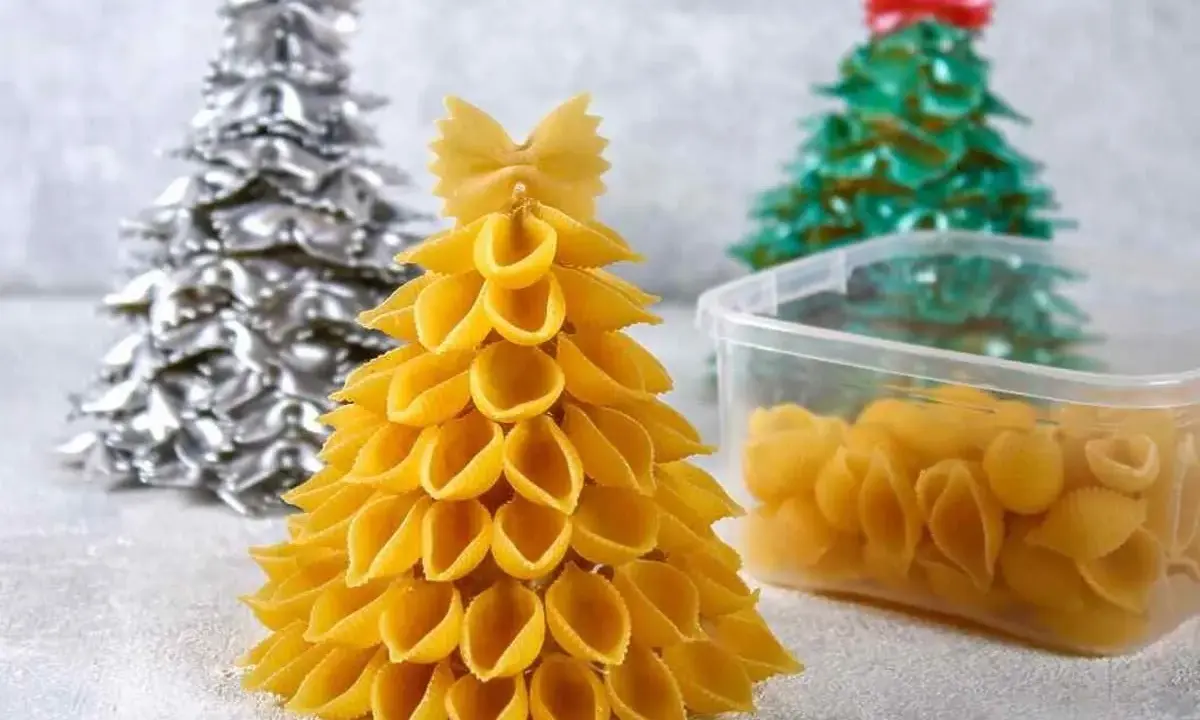 Świąteczne DIY dla dzieci: choinki z makaronu. Złota, srebrna i zielona choinka z różnych rodzajów makaronu, obok pojemnik z muszelkami.