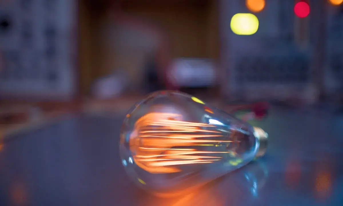 Żarówka LED 8 watt ile to wat? Widoczna żarówka z rozżarzonym żarnikiem, w tle kolorowe światła.