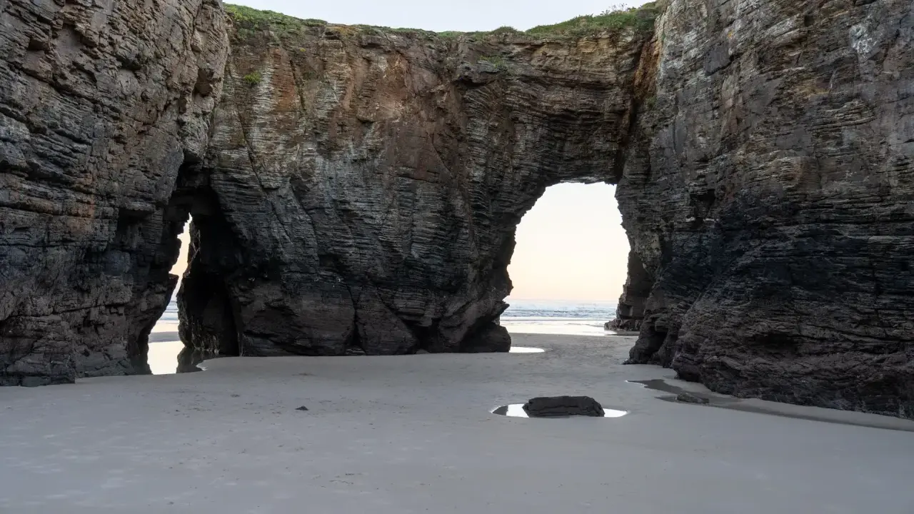 Felsbögen am Praia das Catedrais, die wie Kathedralen wirken, mit Sand und Meer im Hintergrund.
