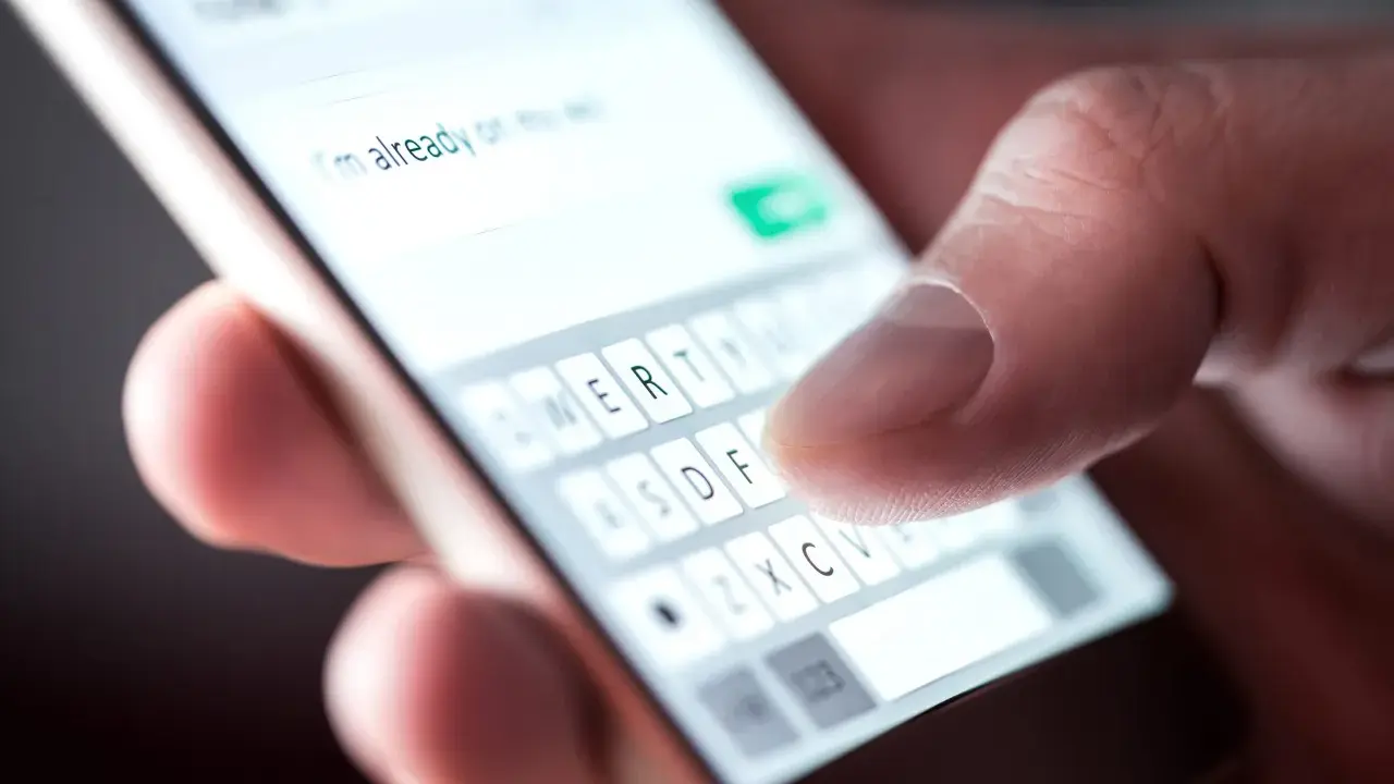 Palec pisze na klawiaturze telefonu, tworząc wiadomość. Widać fragment tekstu "I'm already on my way" i klawisze z literami. To klasyczny przykład polskie znaki w sms.