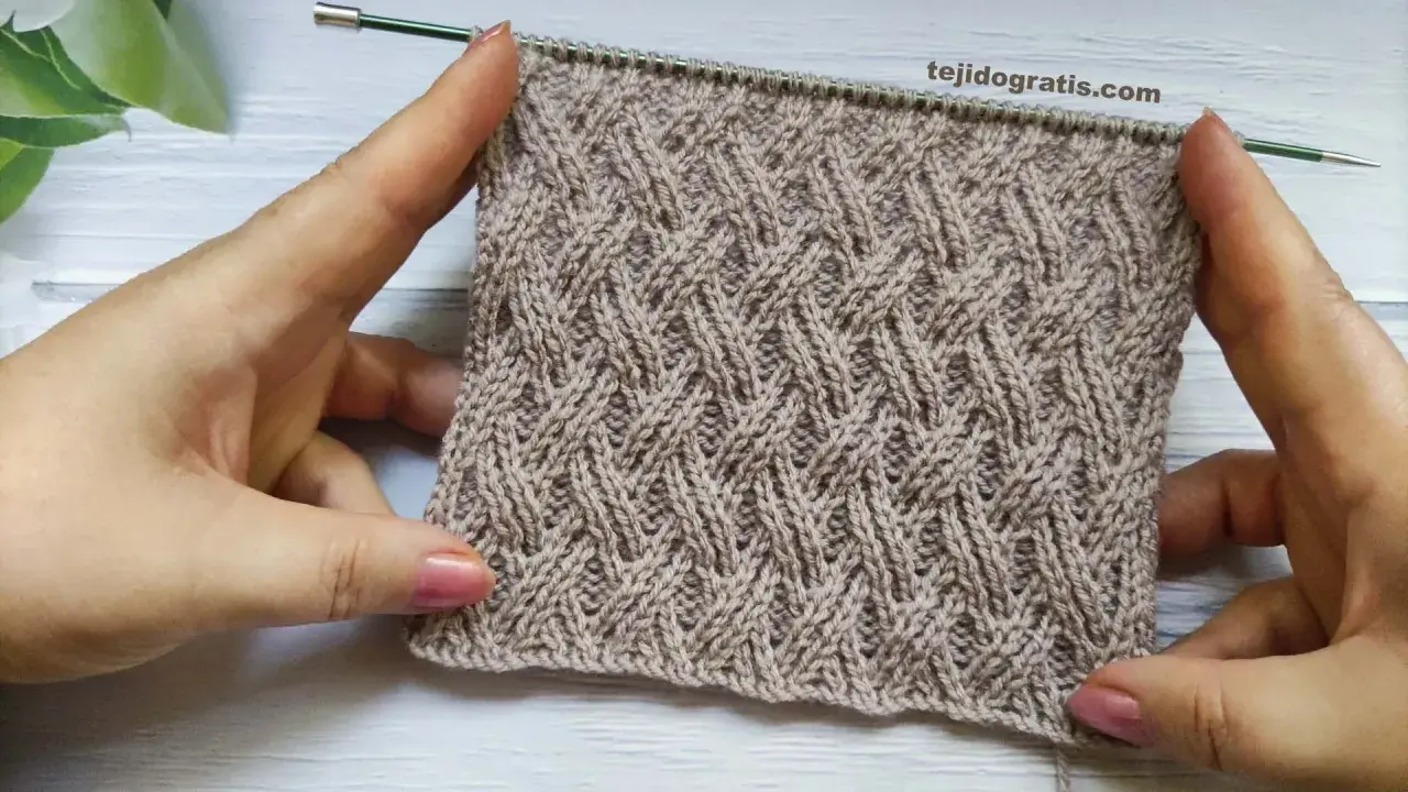Manos sostienen un tejido cruzado de lana beige con un patrón de rombos entrelazados.