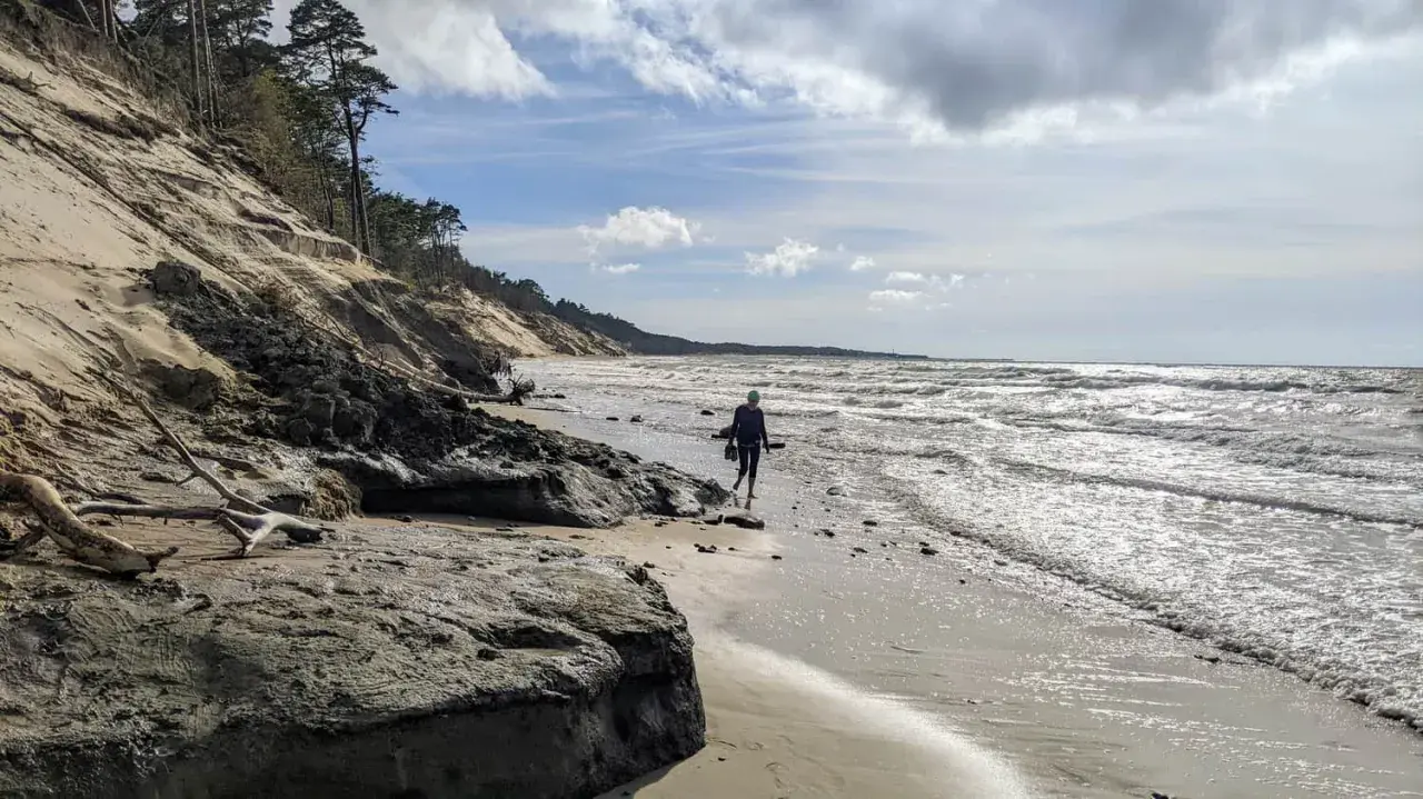 Spacerująca osoba na plaży w Ustce, w oddali widać orzechowo-brązowe klify.