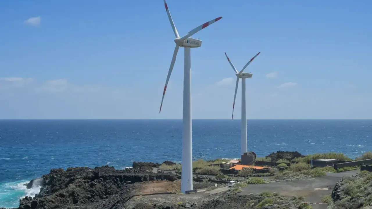 Zwei Windräder an einer felsigen Küste Spaniens, die saubere Energie erzeugen.
