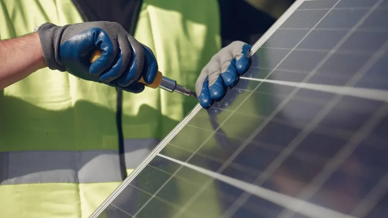 Mains nues, gants bleus et jaunes, tournevis en action pour la réparation d'un panneau solaire.
