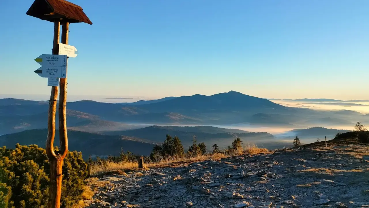 Poranek w Beskidzie Żywieckim. Drewniany drogowskaz wskazuje szlak, a w dole morze mgieł otula doliny.