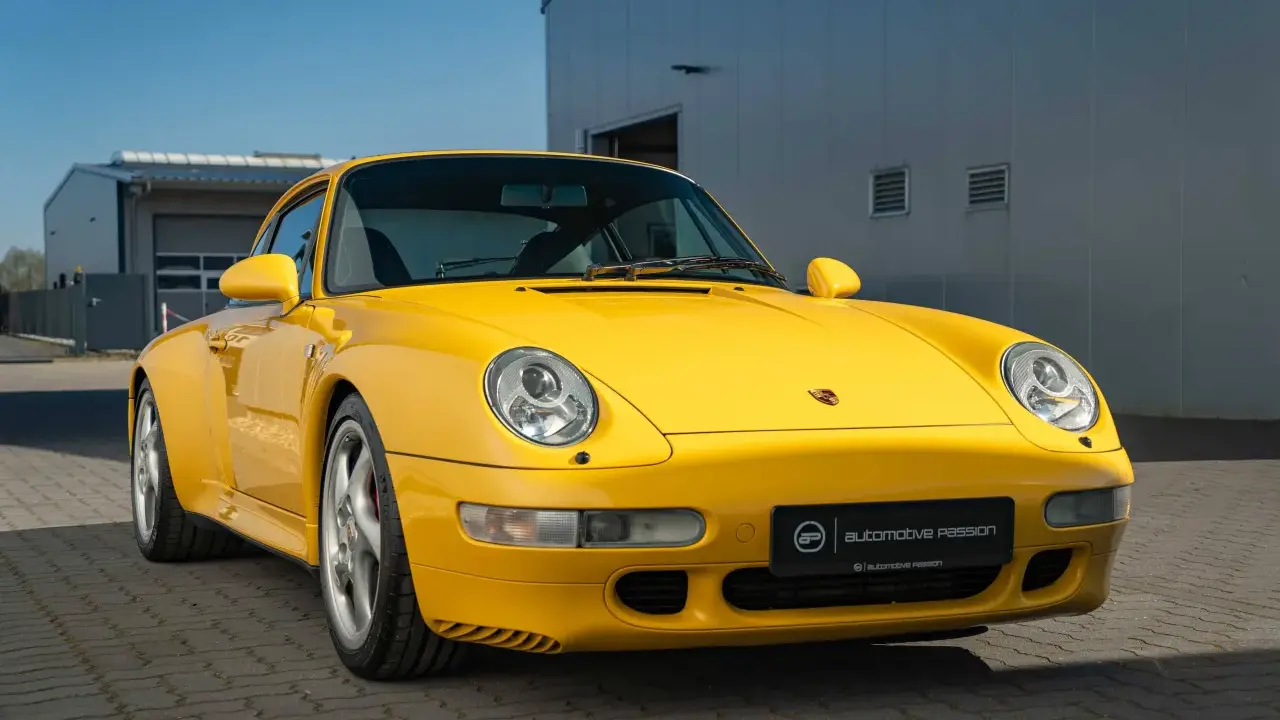 Gelber Porsche 993 vor einem modernen Gebäude. Die Wertentwicklung dieses Klassikers ist bemerkenswert.