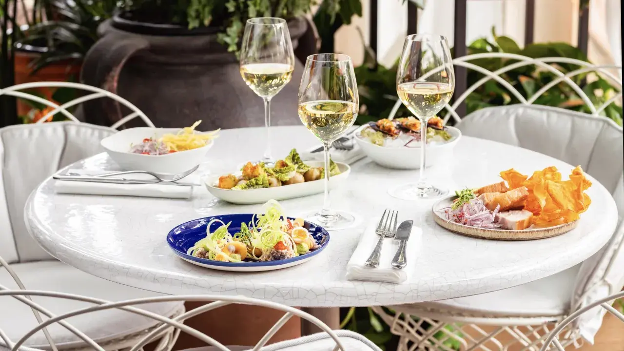 Delicioso brunch con niños en Madrid. Mesa con varios platos, copas de vino blanco y sillas blancas.