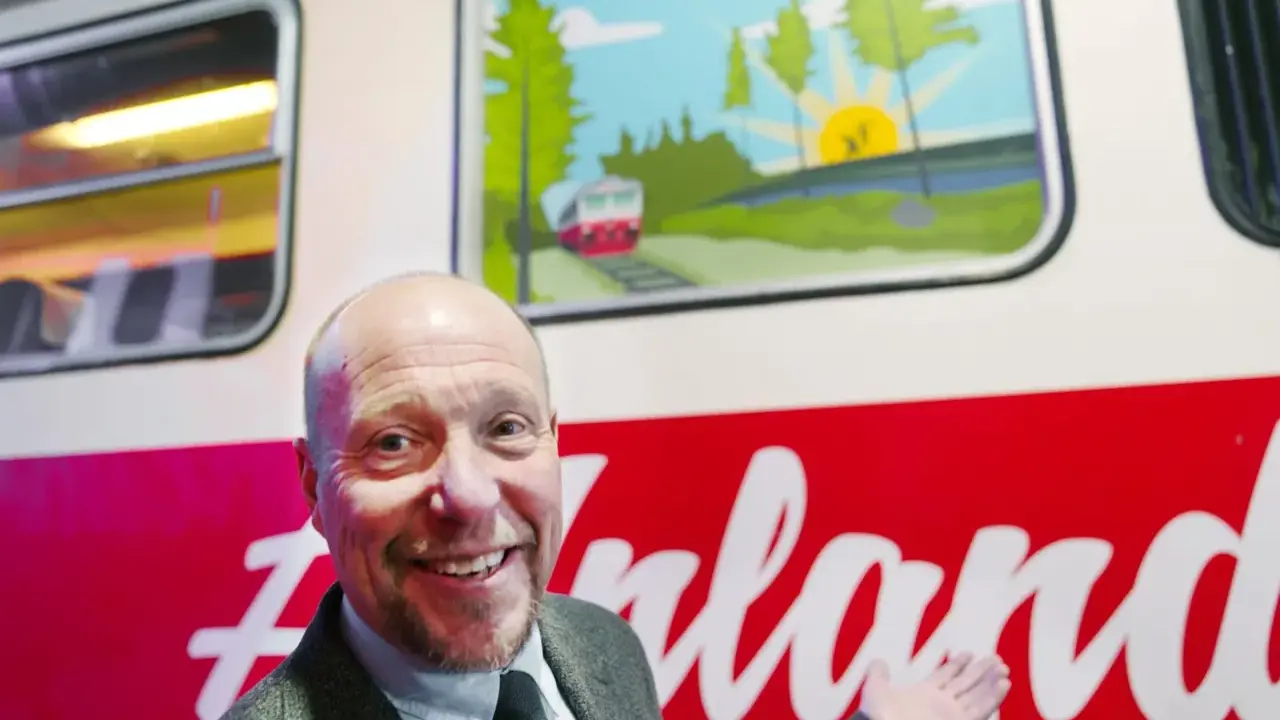 Glad man ler vid en tågvagn med en illustration av ett landskap och ett tåg. Kanske är det ett tåg till Arvidsjaur?