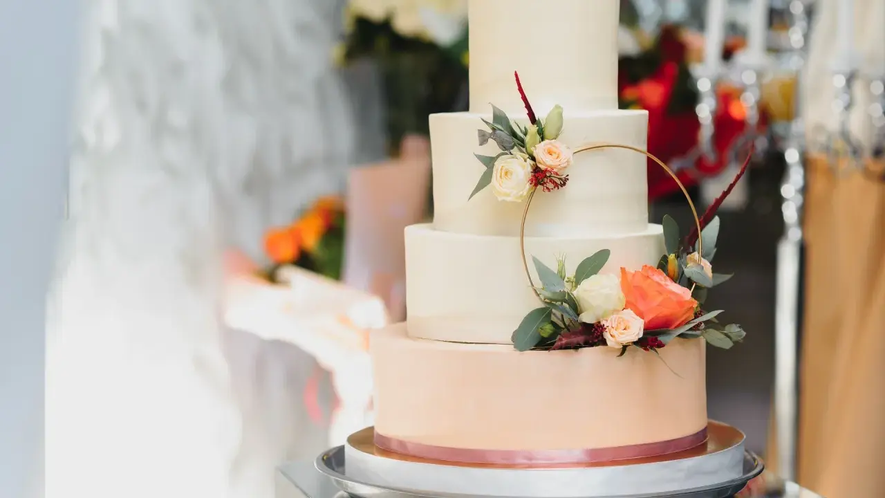 Czteropiętrowy tort weselny w pastelowych kolorach, ozdobiony świeżymi kwiatami i złotym pierścieniem. To najmodniejsze najpiękniejsze torty weselne.