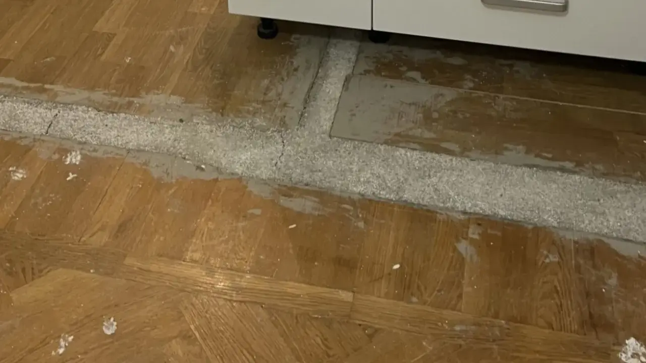 Arbete pågår för att ta bort laminatgolv. Ett vitt pulver och grått material syns på det gamla trägolvet.