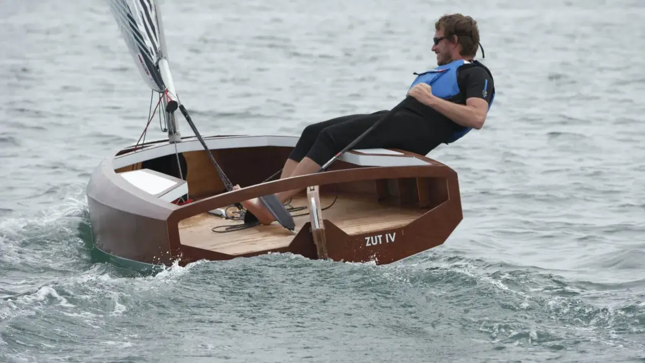 Un homme navigue sur un petit bateau en bois, le "ZUT IV", dans une mer agitée.