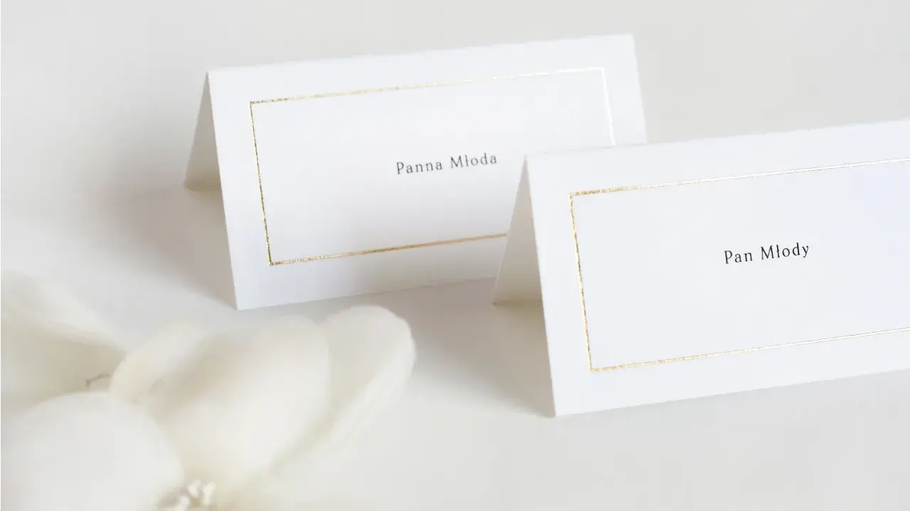 Eleganckie winietki dla pary młodej z subtelną złotą ramką. "Panna Młoda" i "Pan Młody" zapowiadają uroczystość.
