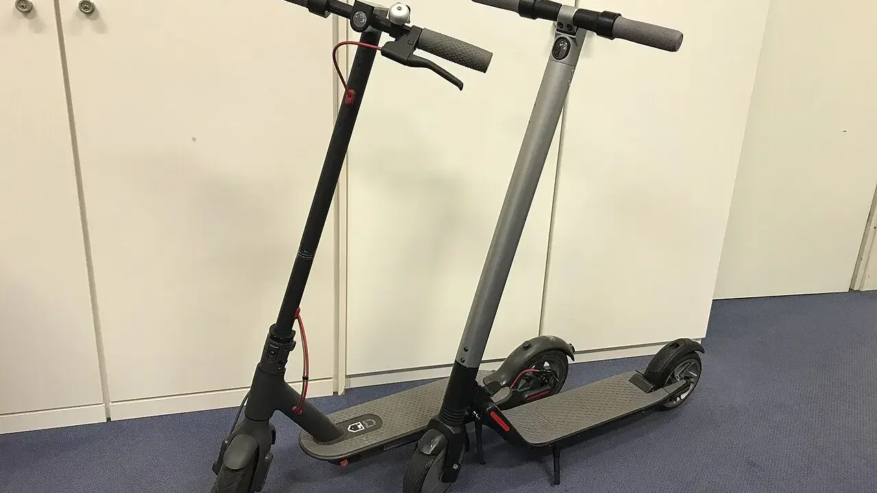 Deux trottinettes électriques, noires et grises, prêtes à l'emploi. La trottinette électrique définition : un moyen de transport urbain pratique.