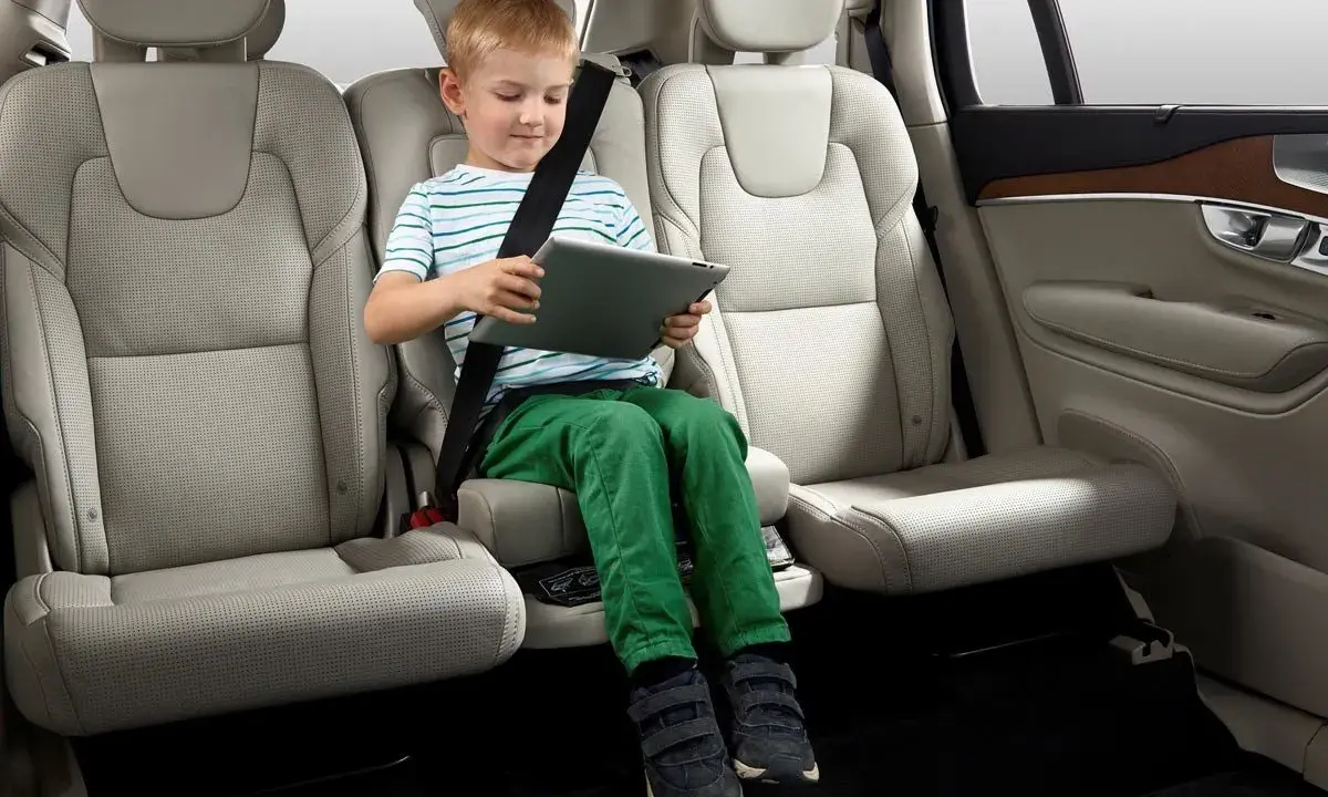 Niño en asiento elevador integrado, con cinturón de seguridad puesto, usando una tablet. ¿Cuál es el asiento más seguro del coche?