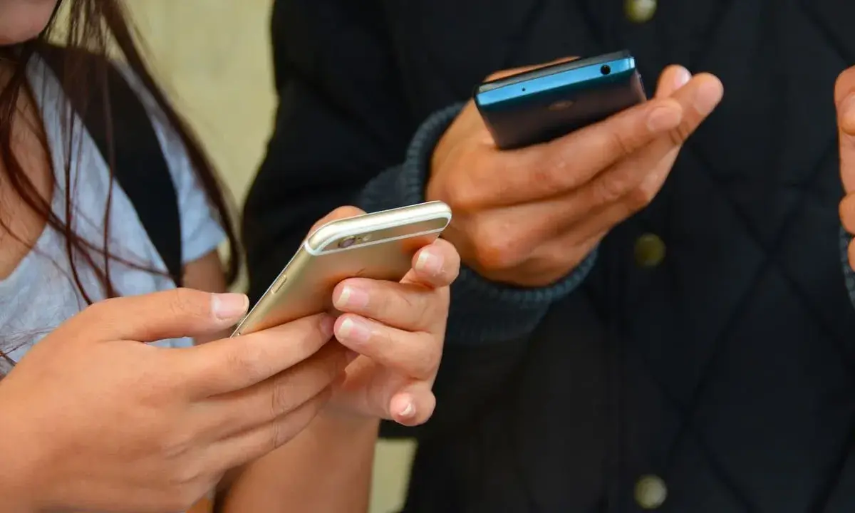 Zwei Hände halten Smartphones. Eine Frau hält ein goldenes iPhone, ein Mann ein blaues Handy. Vielleicht kommen eingehende Anrufe nicht an.