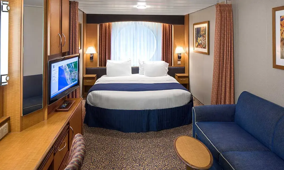 Cabina garantita MSC quando viene assegnata: letto matrimoniale, divano blu, TV e oblò rotondo.