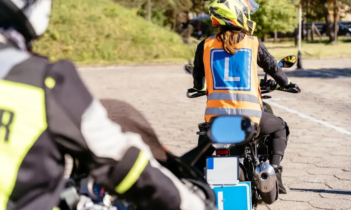 Rozpoczyna się kurs na motocykl. Uczestnicy w kamizelkach z literą "L" ćwiczą jazdę na placu manewrowym.