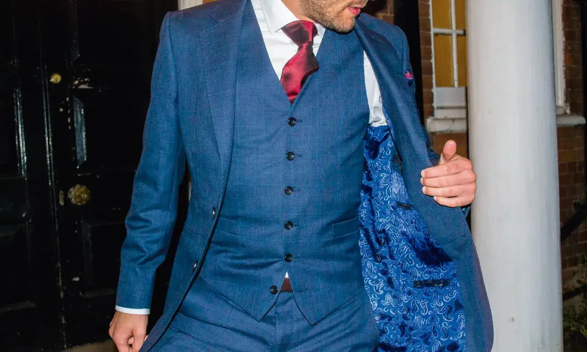 A man in a blue checkered suit, white shirt, and red tie. He's showing off the paisley lining of his jacket, and the bottom button on his vest is unbuttoned.
