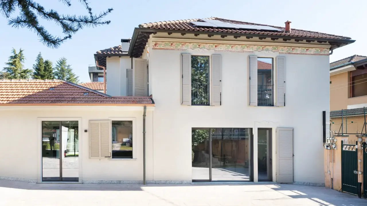 L'abbinamento colori facciata e serramenti crea un'armonia moderna. La casa bianca con dettagli decorativi si fonde con le persiane e gli infissi grigio chiaro.