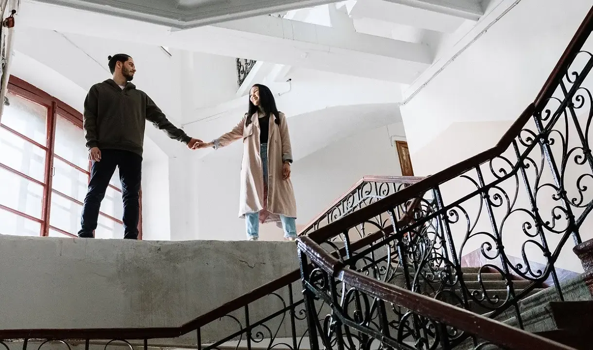 Pareja tomados de la mano en una escalera, ¿qué es ser posesivo? Él la mira, ella sonríe.