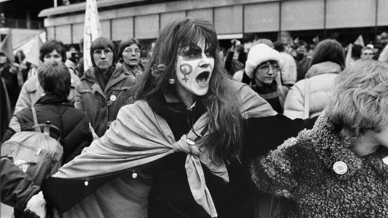 En kvinna med ansiktsmålning och symbolen för kvinnor ropar under en demonstration för sveriges demokratisering.