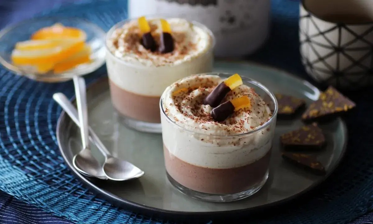 Deux verrines 3 chocolat, garnies de crème fouettée, de copeaux de chocolat et d'écorces d'orange confites.