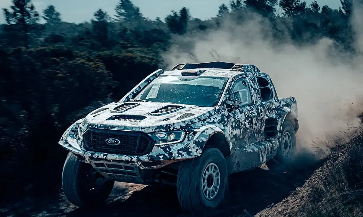 Un Ford Raptor Dakar camuflado levanta polvo en un terreno agreste.