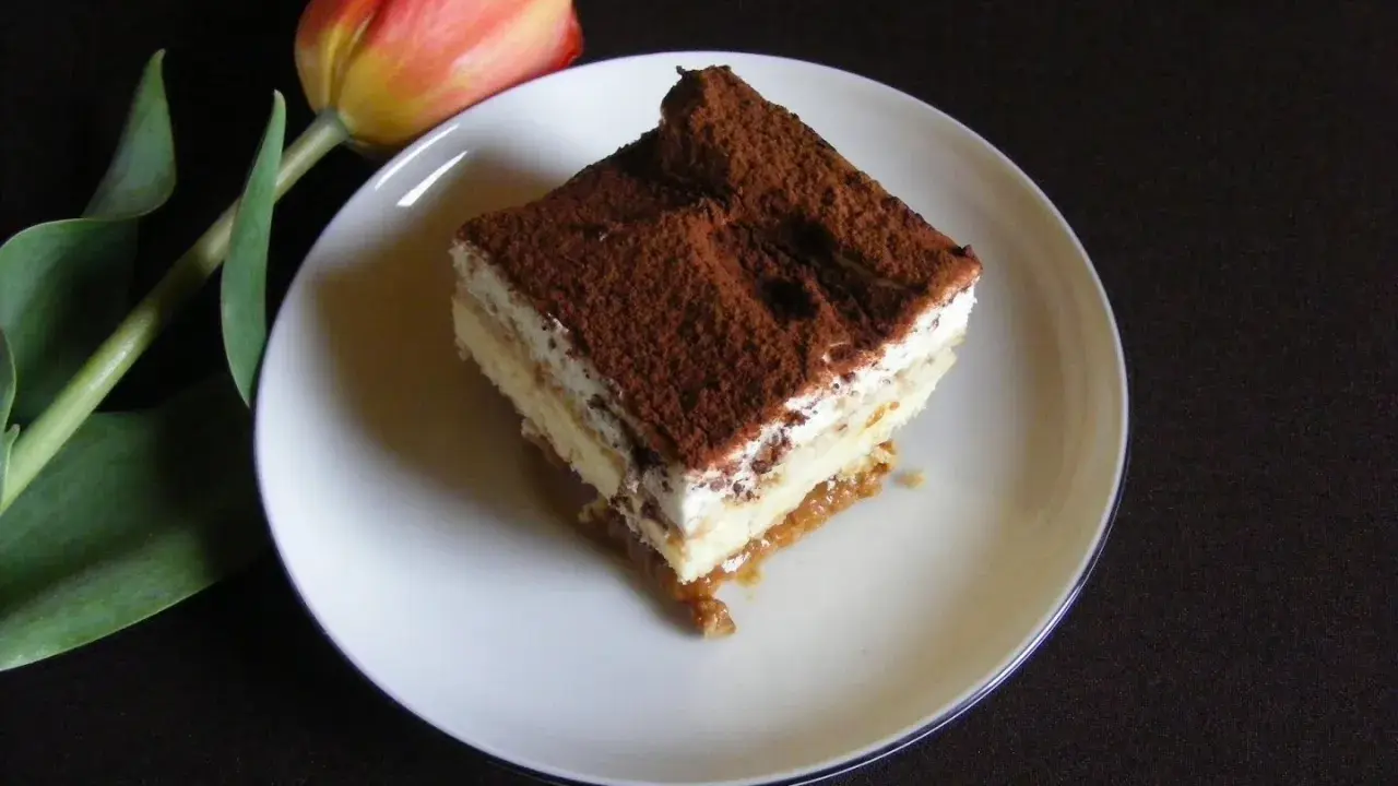 Pyszny kawałek tiramisu, jednego z 10 ciast bez pieczenia, obok czerwonego tulipana.