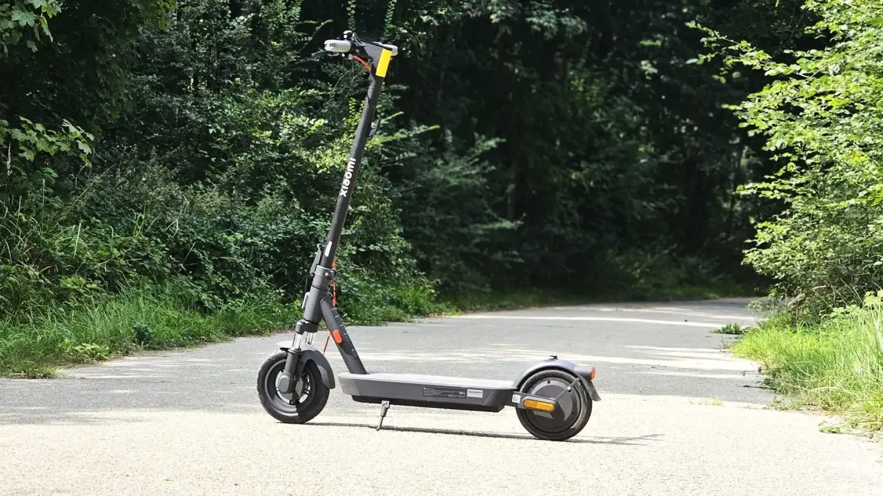 Trottinette Xiaomi grise sur une route asphaltée, entourée de verdure. Parfait pour explorer la nature et profiter de son autonomie.