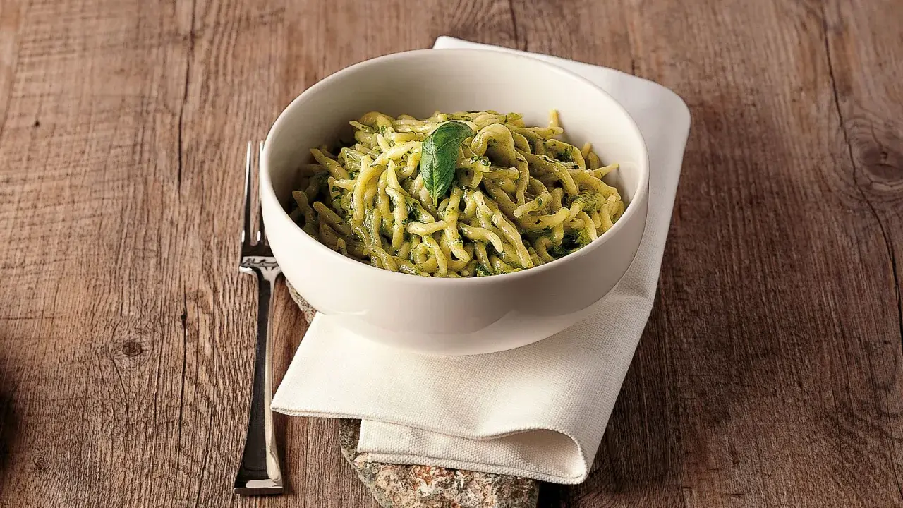 Un piatto invitante di trofie al pesto, guarnito con una foglia di basilico, su un tavolo di legno rustico.