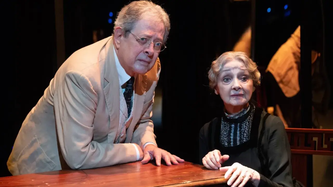 La signora Frola e il signor Ponza, suo genero, si guardano con espressione preoccupata, appoggiati a un tavolo di legno scuro.