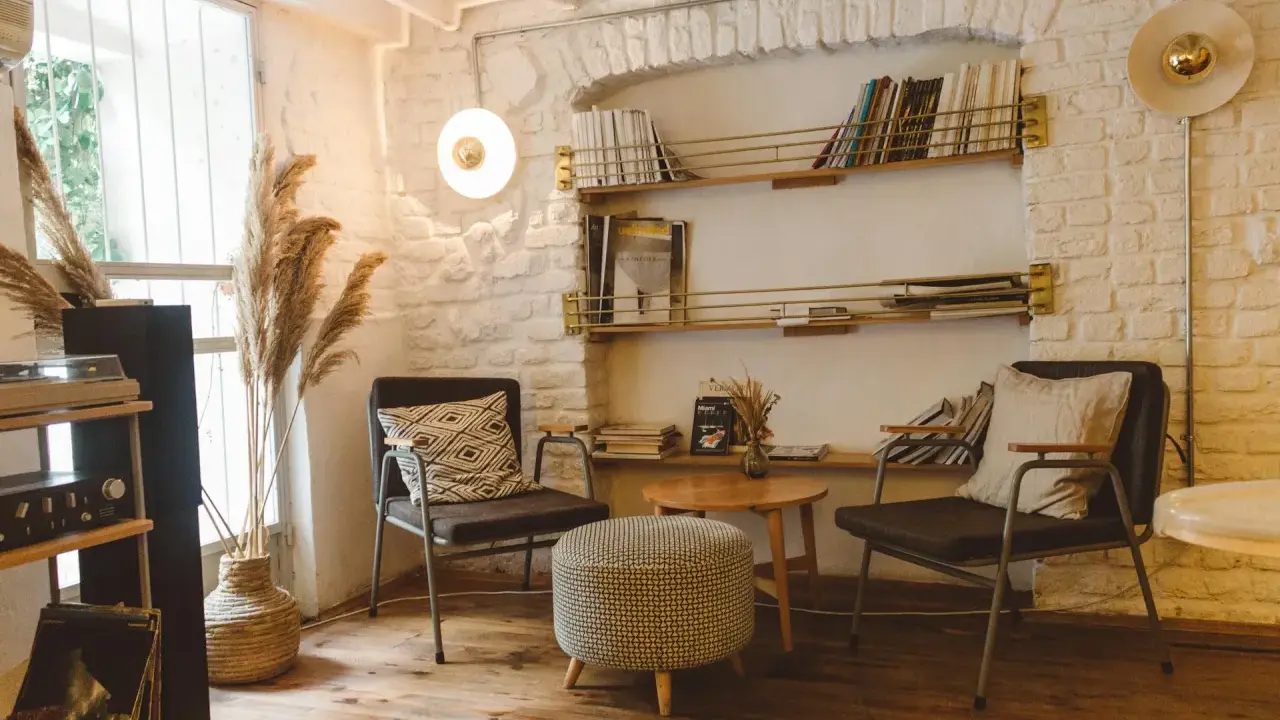 Acogedor rincón de lectura con sillas cómodas, mesa auxiliar, estanterías llenas de libros y plantas secas.