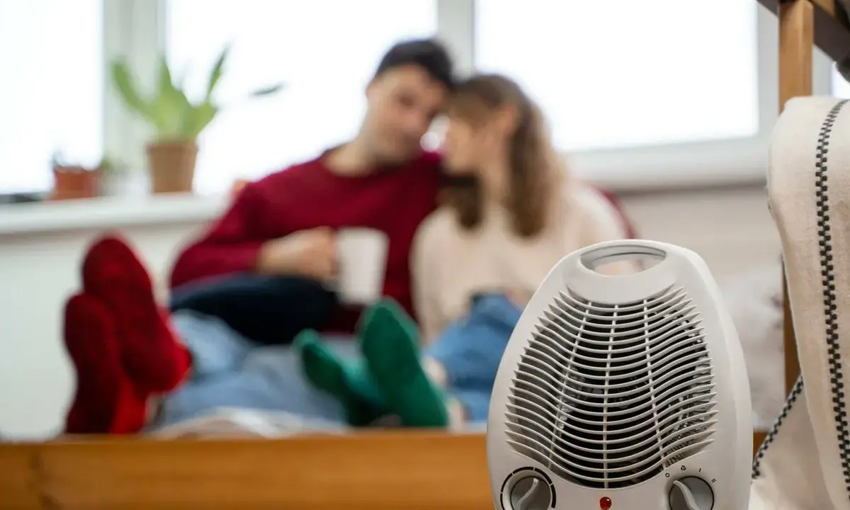 Pareja acurrucada con bebidas calientes, un radiador eléctrico en primer plano. Así funciona un radiador eléctrico para calentar el hogar.