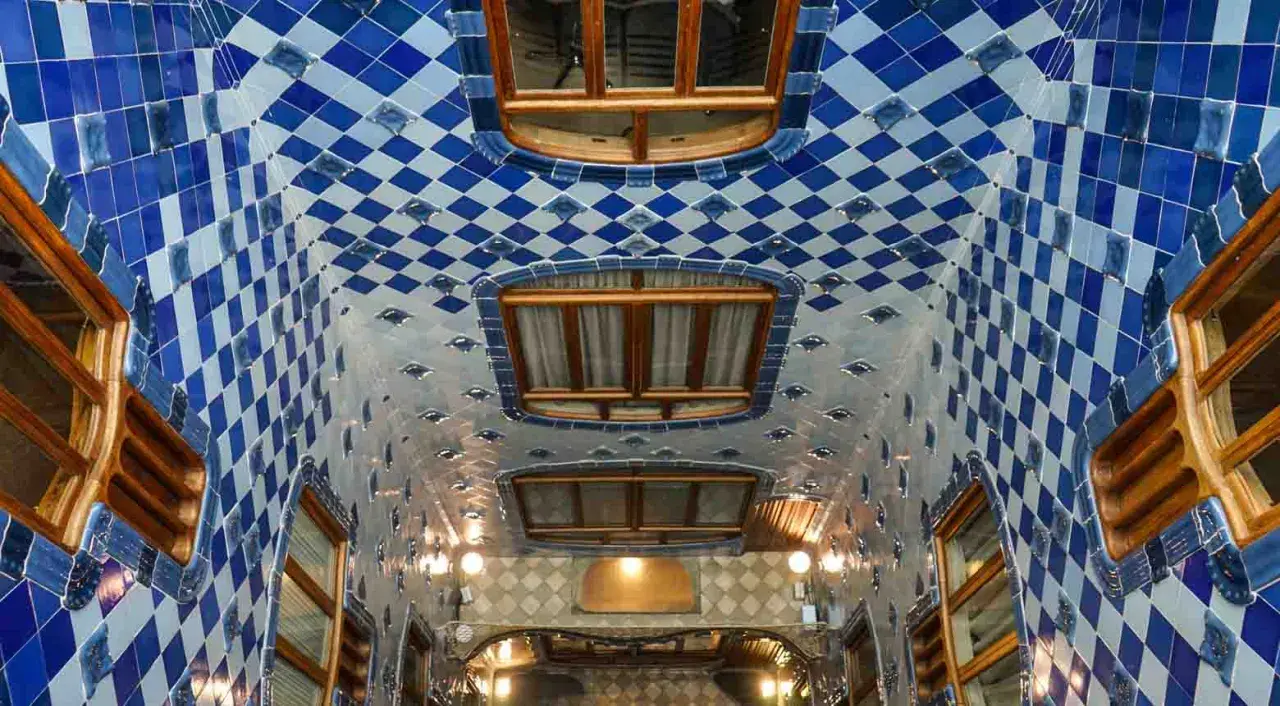 Interno della Casa Batlló: soffitto ondulato con piastrelle blu e bianche a rombi, finestre in legno e luci soffuse.