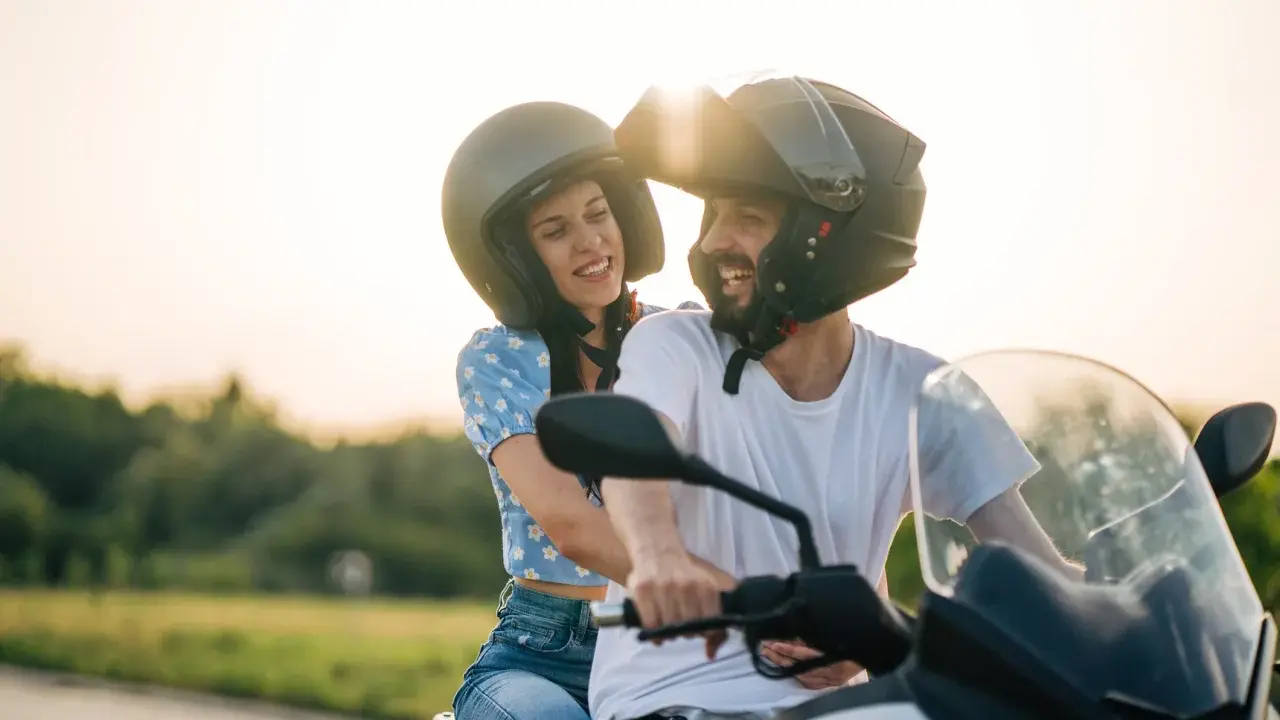 Pareja feliz en moto, disfrutando del atardecer. El sol brilla sobre sus cascos, creando un ambiente de aventura y libertad. CSRNET A2.