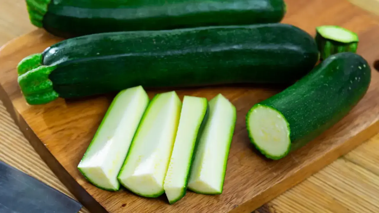 Courgettes vertes entières et coupées en bâtonnets sur une planche à découper, prêtes à congeler.