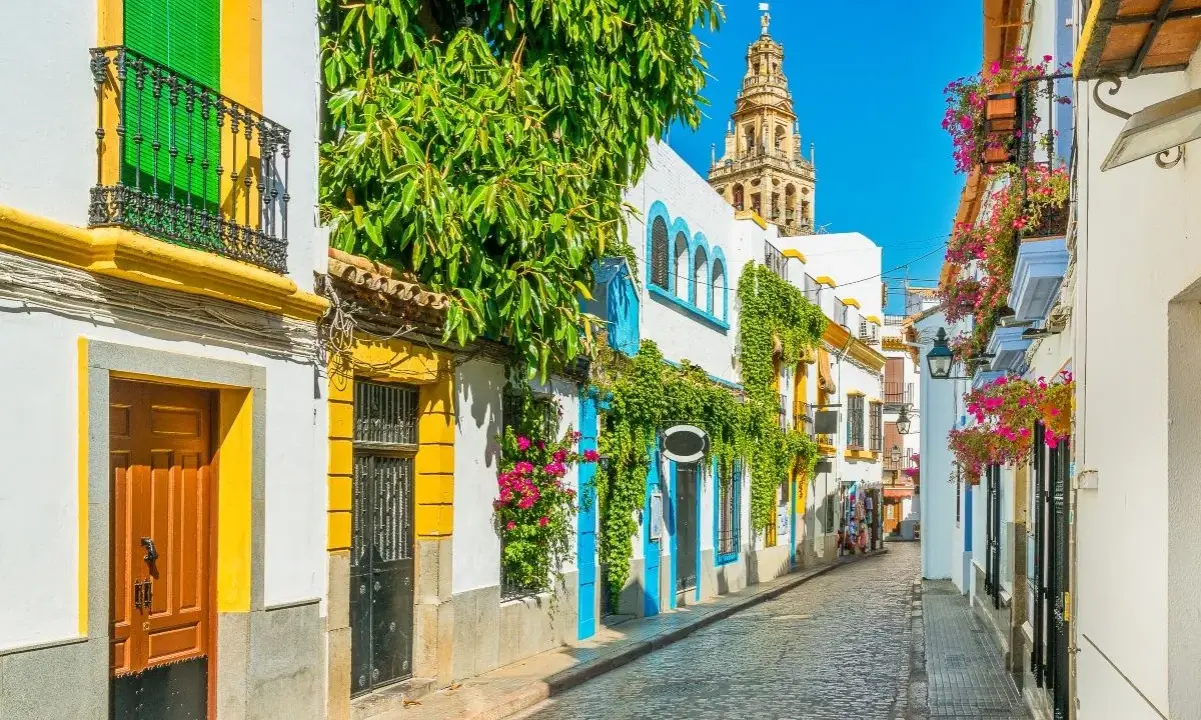 Calle empedrada con casas blancas adornadas con flores y enredaderas. Al fondo, la torre de la Mezquita-Catedral, un imprescindible que ver en Andalucía.
