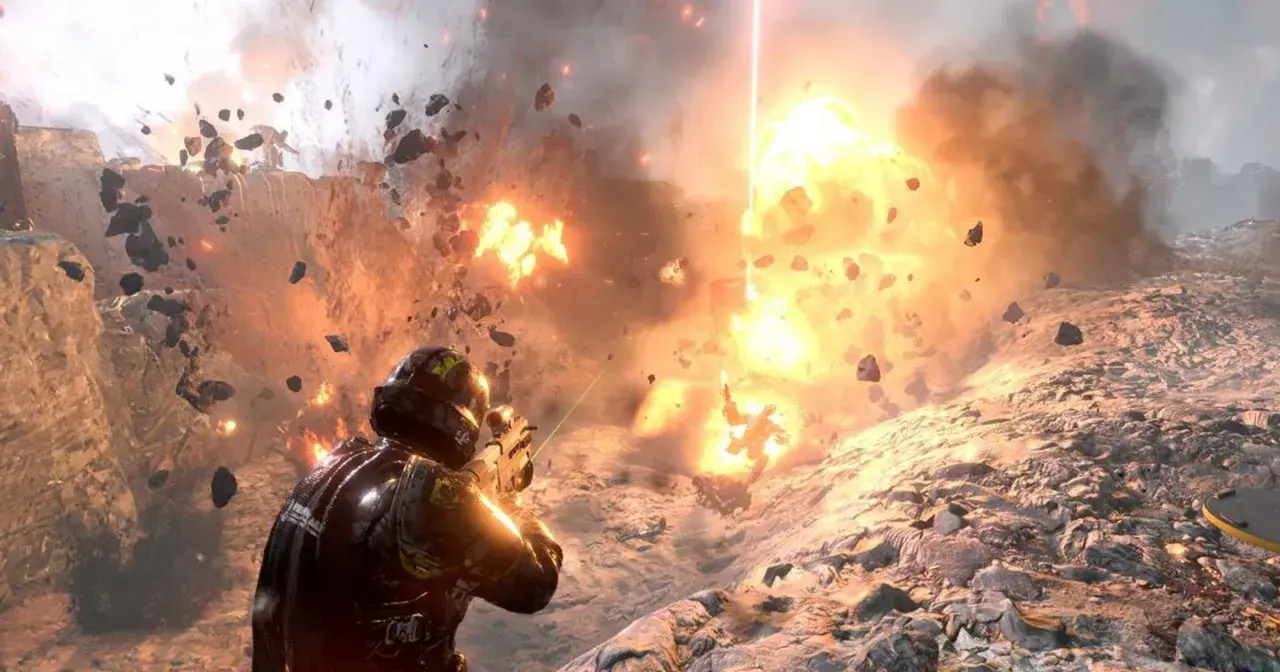 Żołnierz w zbroi walczy w ogniu eksplozji, odłamki skał latają wokół. To scena z gry Helldivers 2.