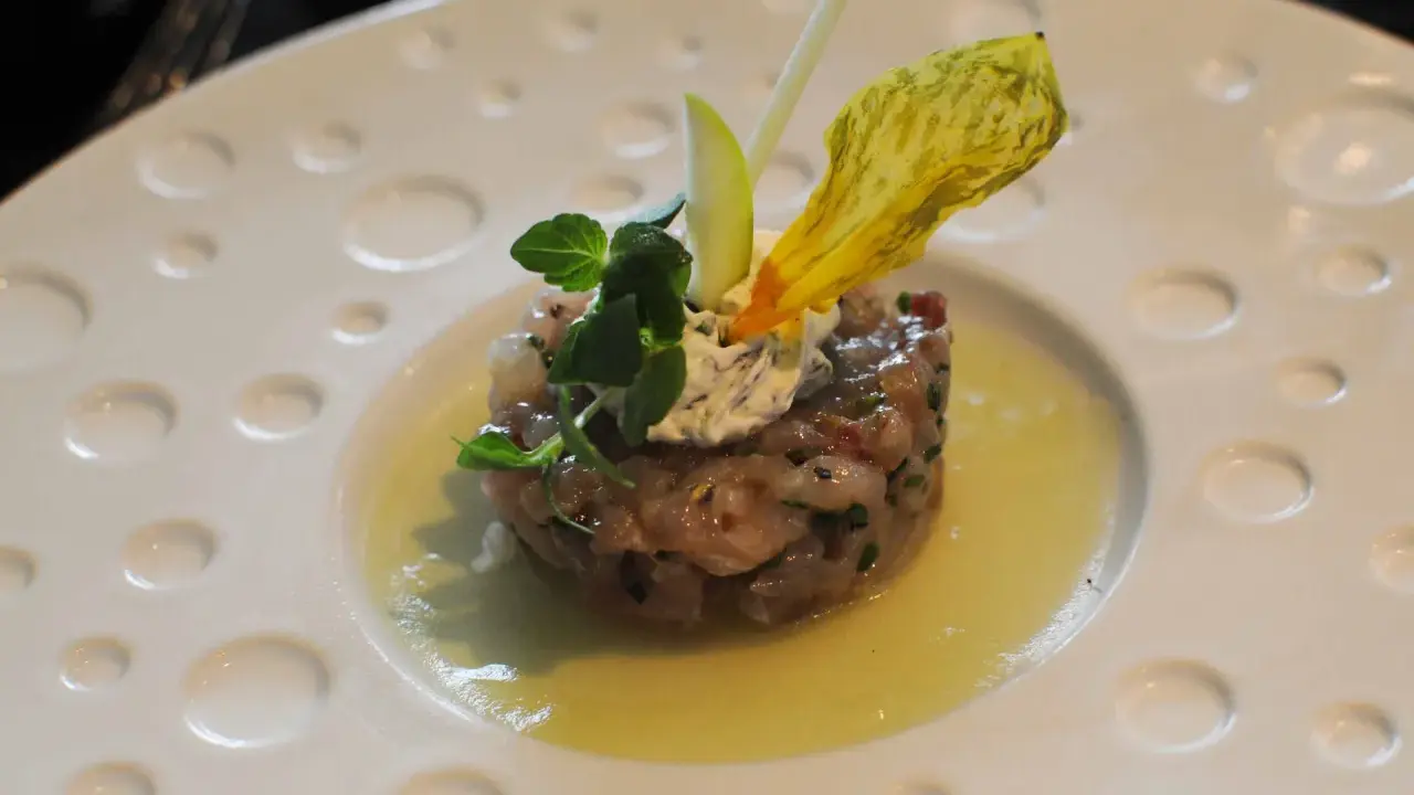 Un tartare de poisson finement préparé, garni de crème, herbes fraîches et d'une fleur jaune, une des spécialités Limoges.