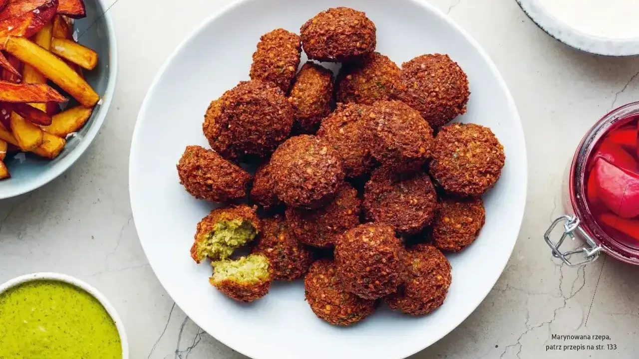 Talerz pełen chrupiących kuleczek, które są idealnym przykładem tego, co to jest falafel. Podane z zielonym sosem i frytkami.