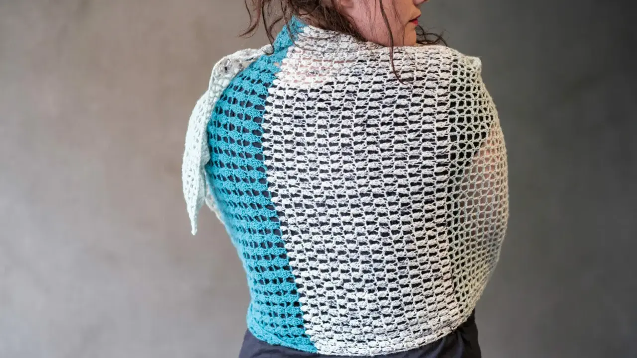 Mujer de espaldas con un cubre hombros a crochet de dos colores, blanco y azul turquesa, con un diseño calado.