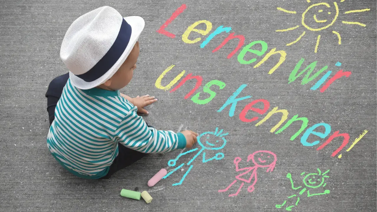 Kleiner Junge mit Hut malt mit Kreide auf Asphalt. Namensspiele für Kinder: "Lernen wir uns kennen!" mit Sonne und Figuren.