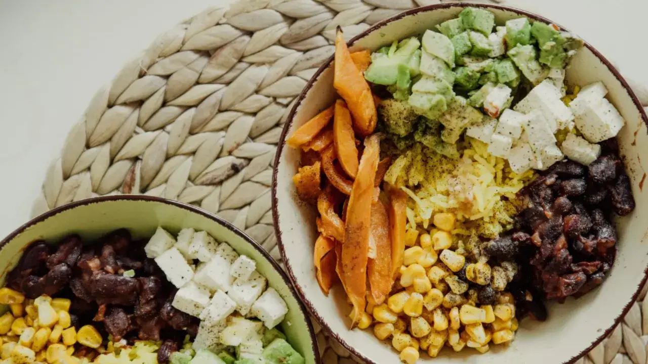 Zwei Schüsseln mit gesunden Reis Rezepten zum Abnehmen: Reis, Bohnen, Mais, Süßkartoffeln, Avocado und Feta.