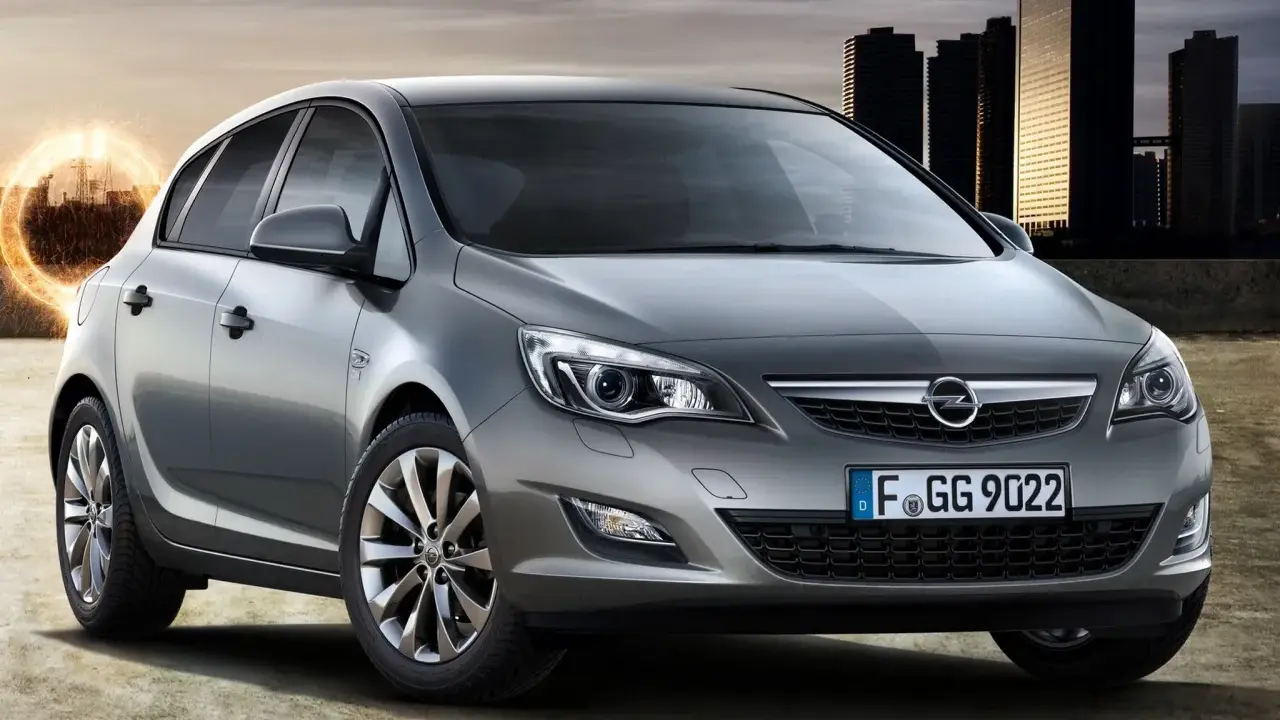 Szary Opel Astra J 1.7 CDTI z nowoczesnymi światłami i felgami, na tle miasta i energetycznego kręgu.