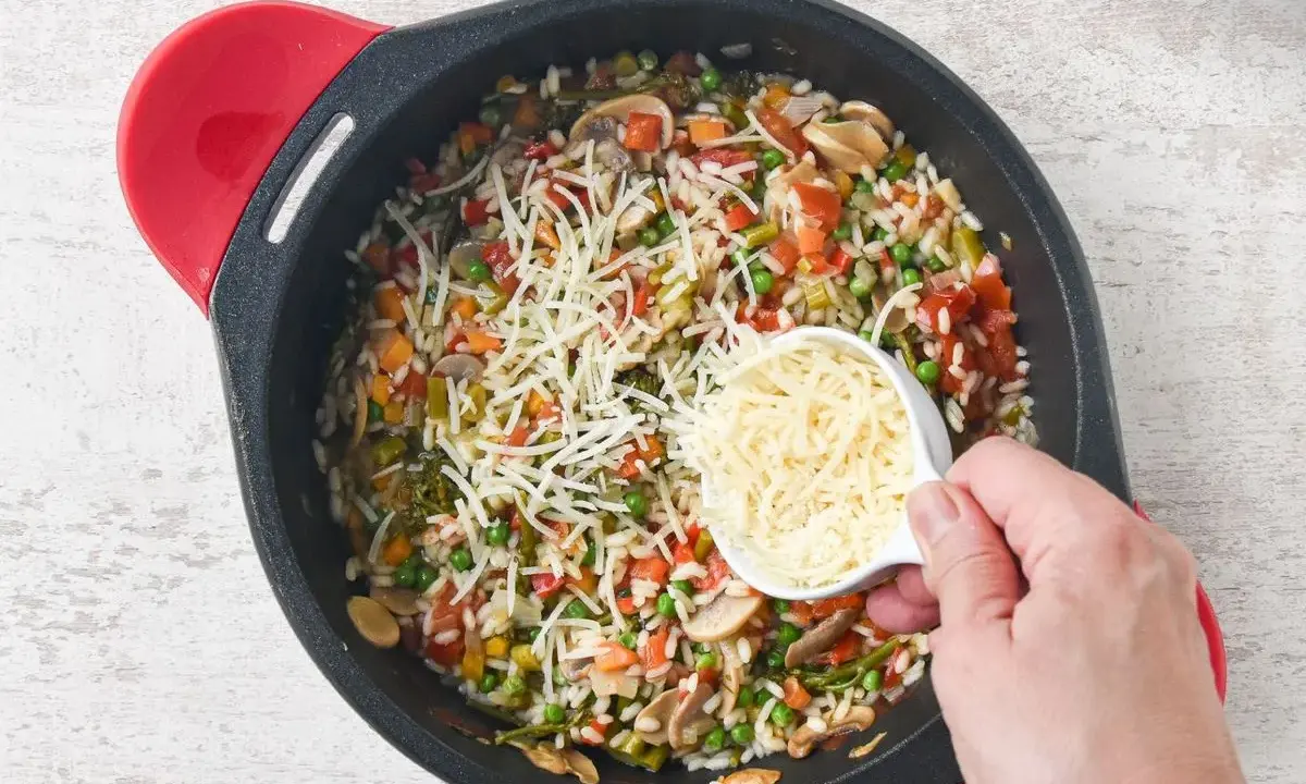 Un delicioso risotto de verduras en una sartén, con queso rallado a punto de ser añadido.