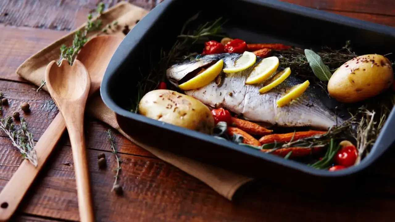 Pescado al horno con patatas, zanahorias y tomates, listo para servir.