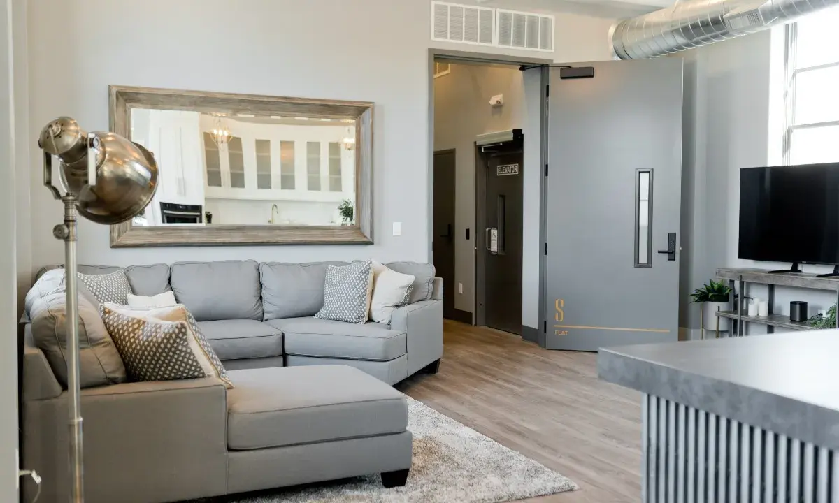 A grey sectional sofa with patterned pillows sits on a rug in a modern living room.